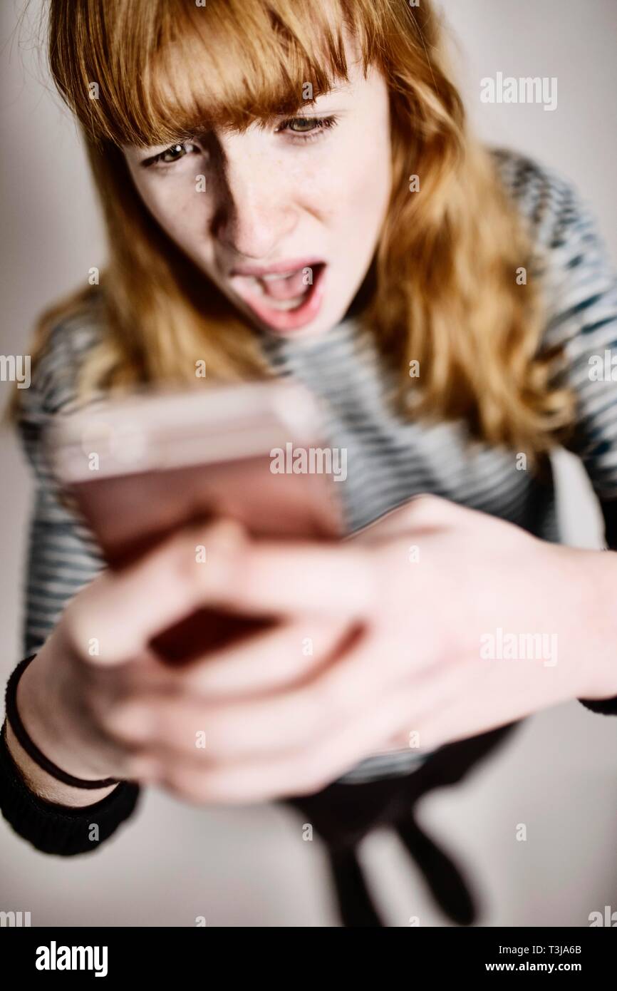 Niña, adolescente, pelirrojo, mira horrorizado en su smartphone, Foto de estudio, Alemania Foto de stock