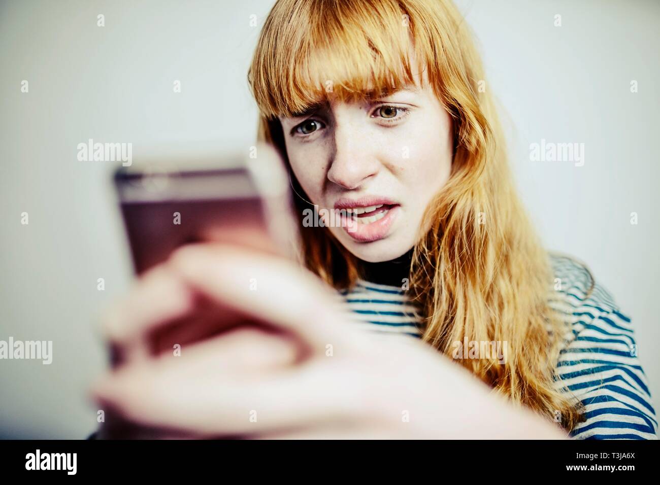 Niña, adolescente, pelirrojo, mira horrorizado en su smartphone, Foto de estudio, Alemania Foto de stock