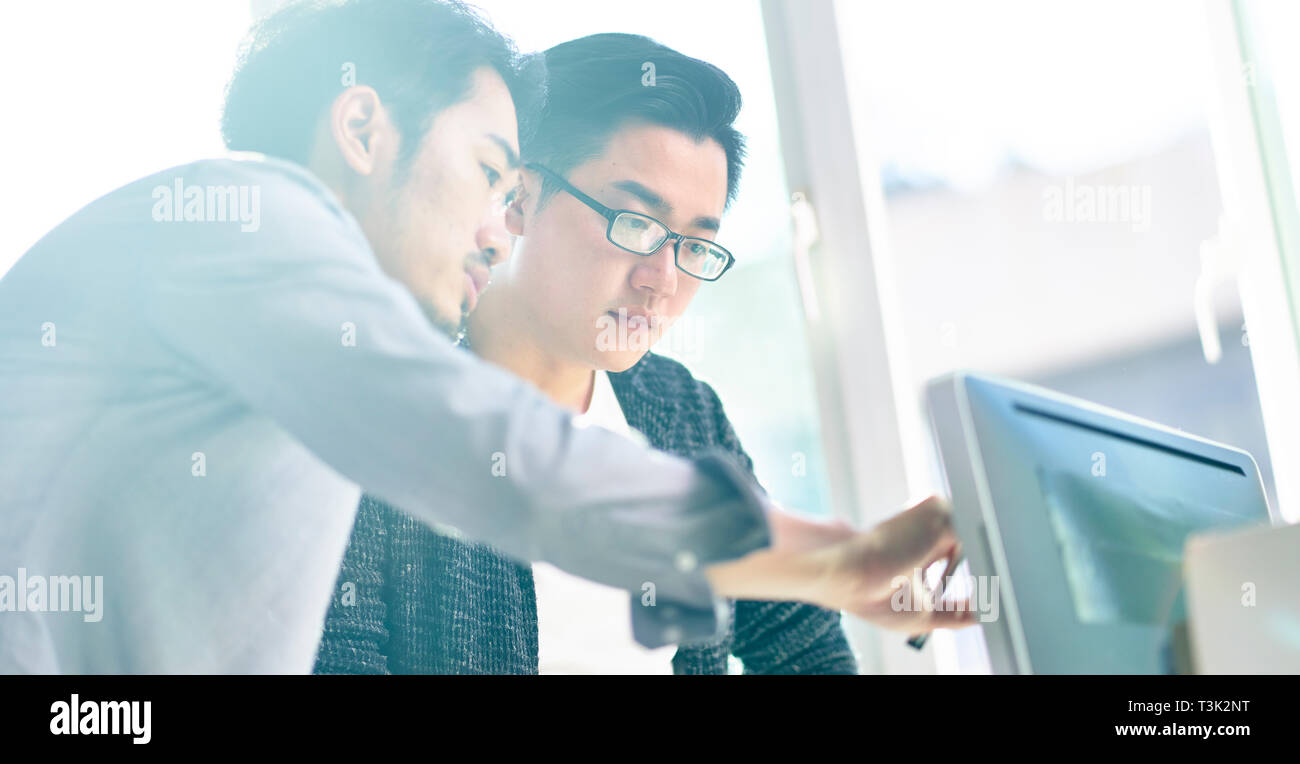 Dos jóvenes ejecutivos de empresas asiáticas que trabajan junto con el ordenador de sobremesa. Foto de stock