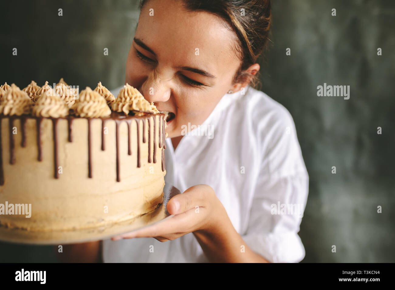 Chef femenina comer todo el pastel. Chef sosteniendo un gran pastel en la mano y tomar un bocado. Foto de stock