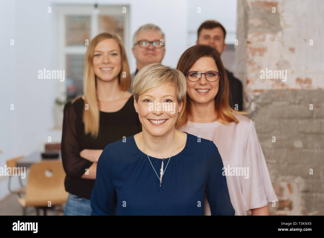 Small Business team foto de grupo con pelo corto, suéter de Mujer en azul  en la parte delantera. La gente de pie en la oficina detrás de la otra,  mirando a la