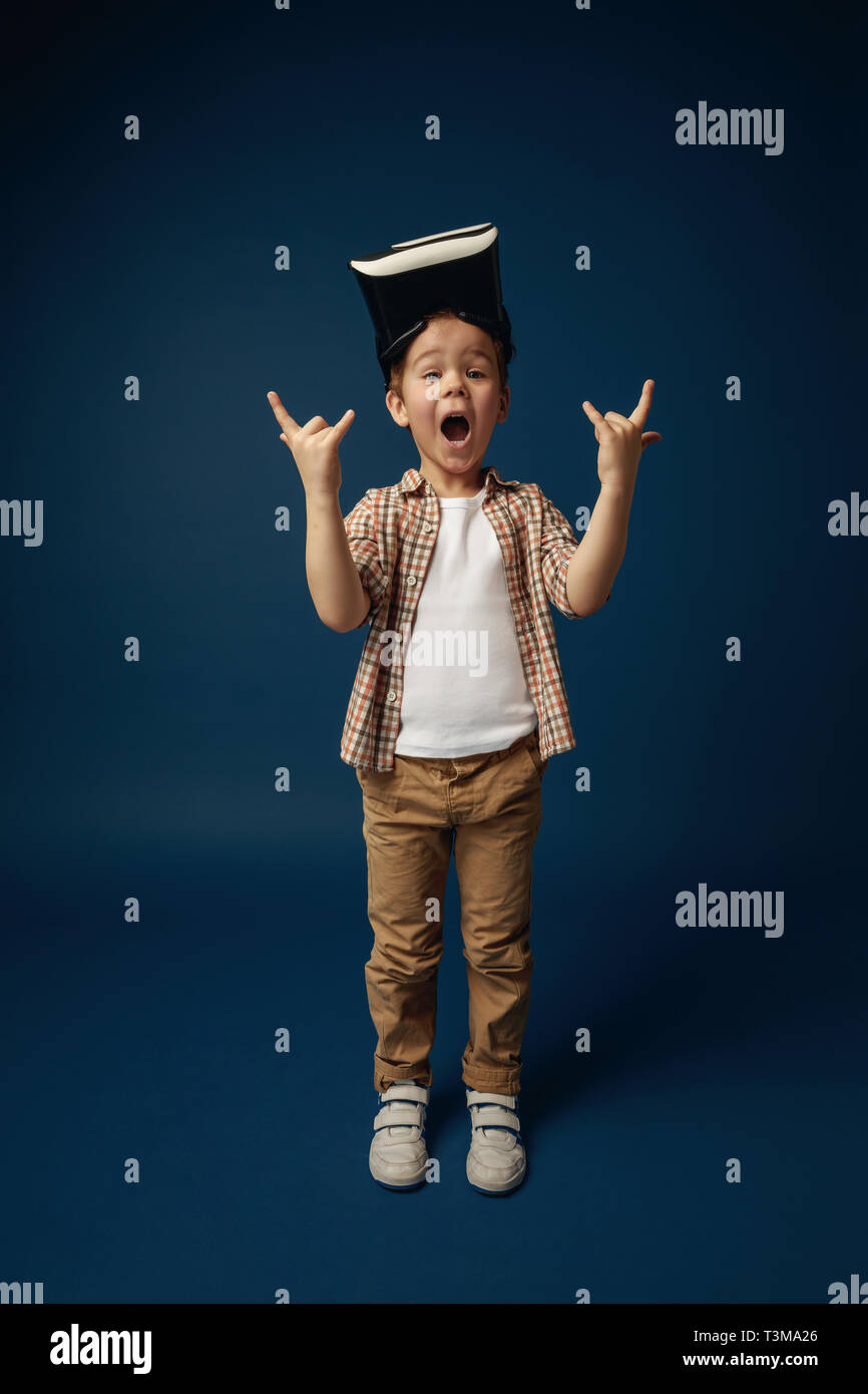 Preguntándose y gritando. Chico o niño en pantalones vaqueros y camisa con casco de realidad virtual gafas aislado sobre fondo azul studio. Concepto de tecnología de vanguardia, video juegos, innovación. Foto de stock