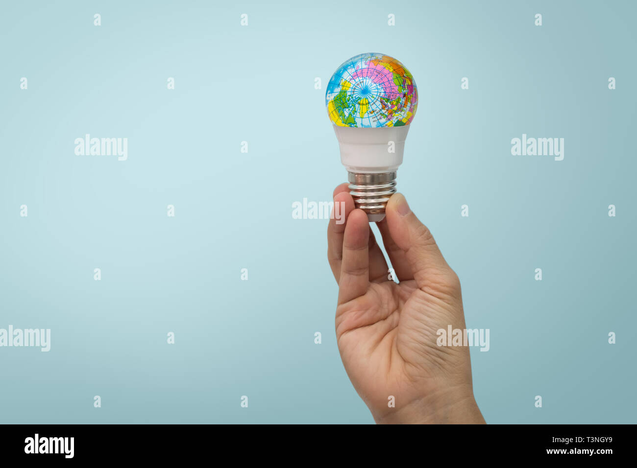 La mano sujeta la bombilla LED con el globo sobre fondo azul. Foto de stock