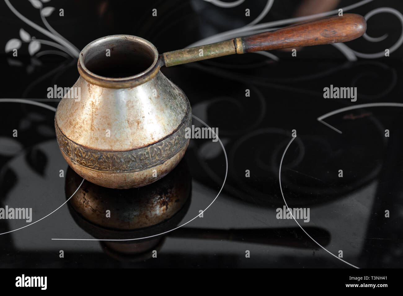 Bronce antiguo retro turco cafetera kanaka sobre vidrio vitrocerámica y  horno con mango de madera, desgastada sobre un fondo negro en un  apartamento en la cocina. Ret Fotografía de stock - Alamy