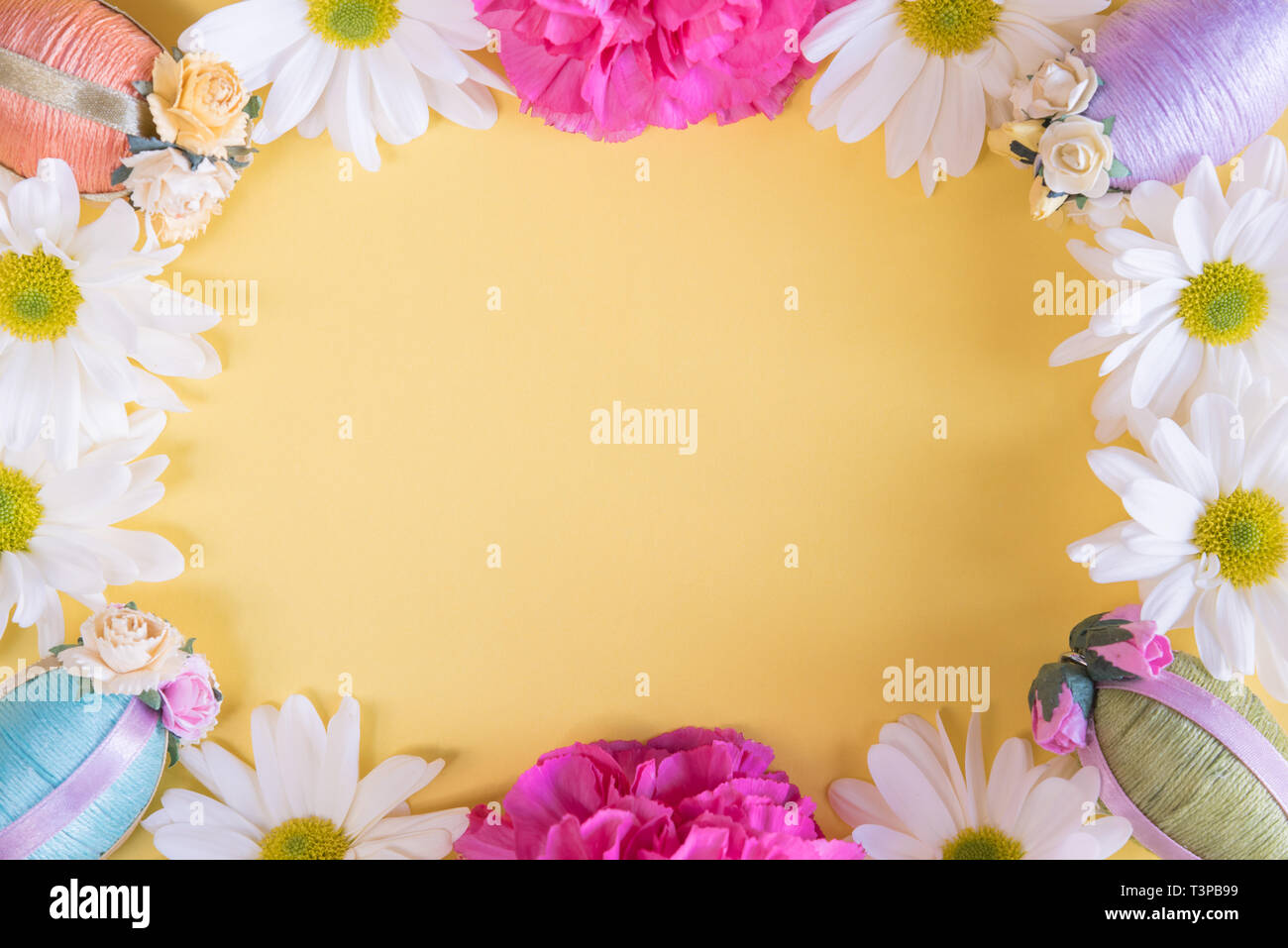 Bastidor de laicos plana de huevos de Pascua y flores sobre fondo amarillo pastel sólido Foto de stock
