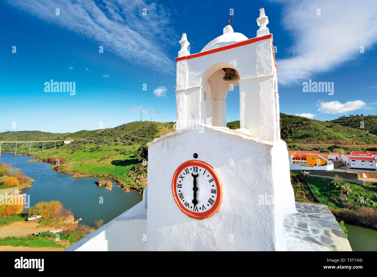 Torre del reloj blanco brillante con vistas a río con colinas verdes en un día soleado Foto de stock