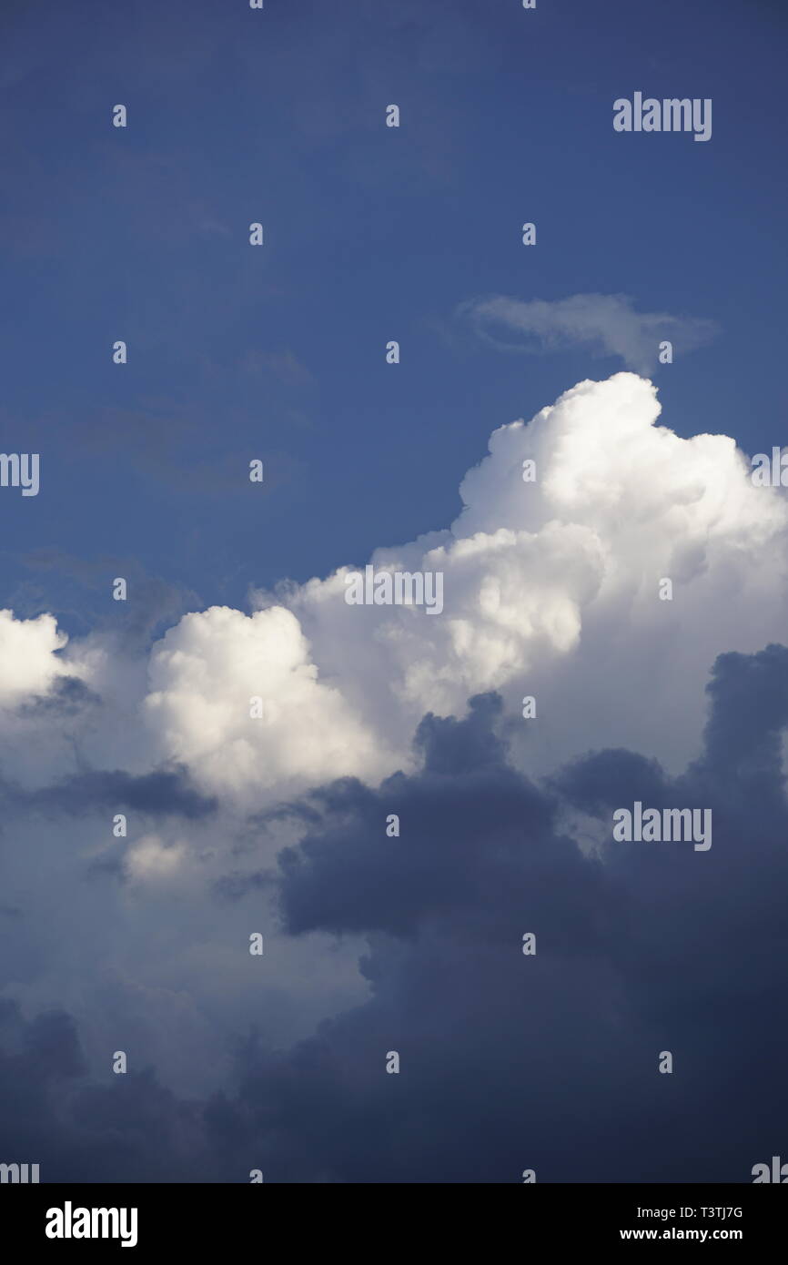Capas de nubes blancas mullidas y gris oscuro, delante de un cielo azul Foto de stock