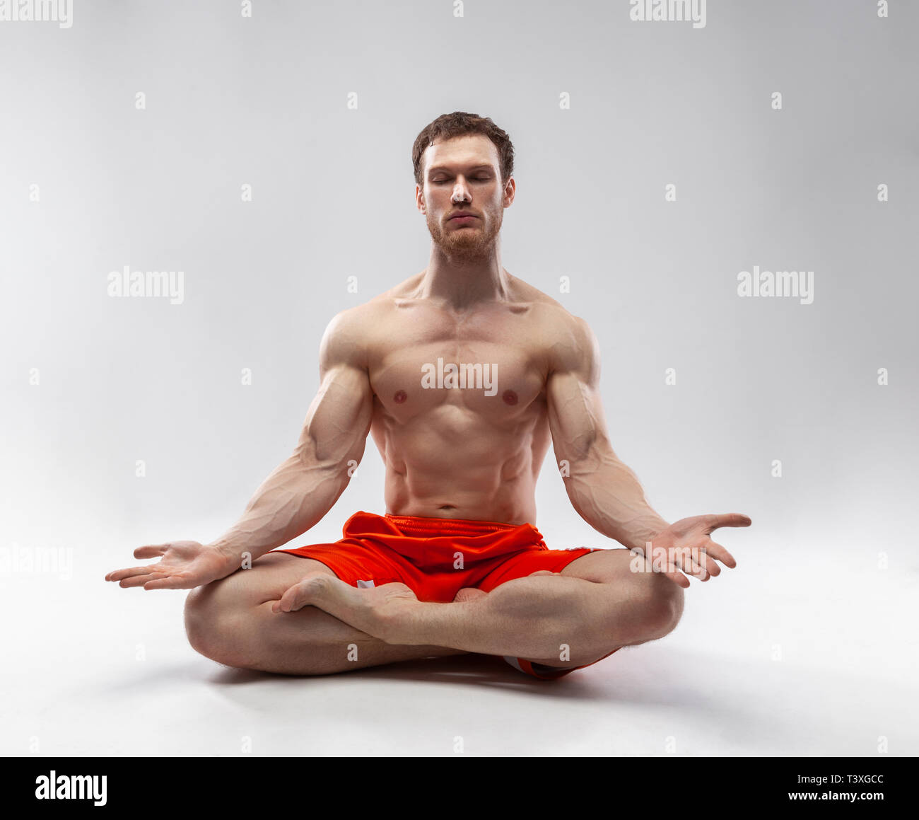 Un hombre con sus ojos cerrados y el cuerpo musculoso sentado en la postura del loto Foto de stock