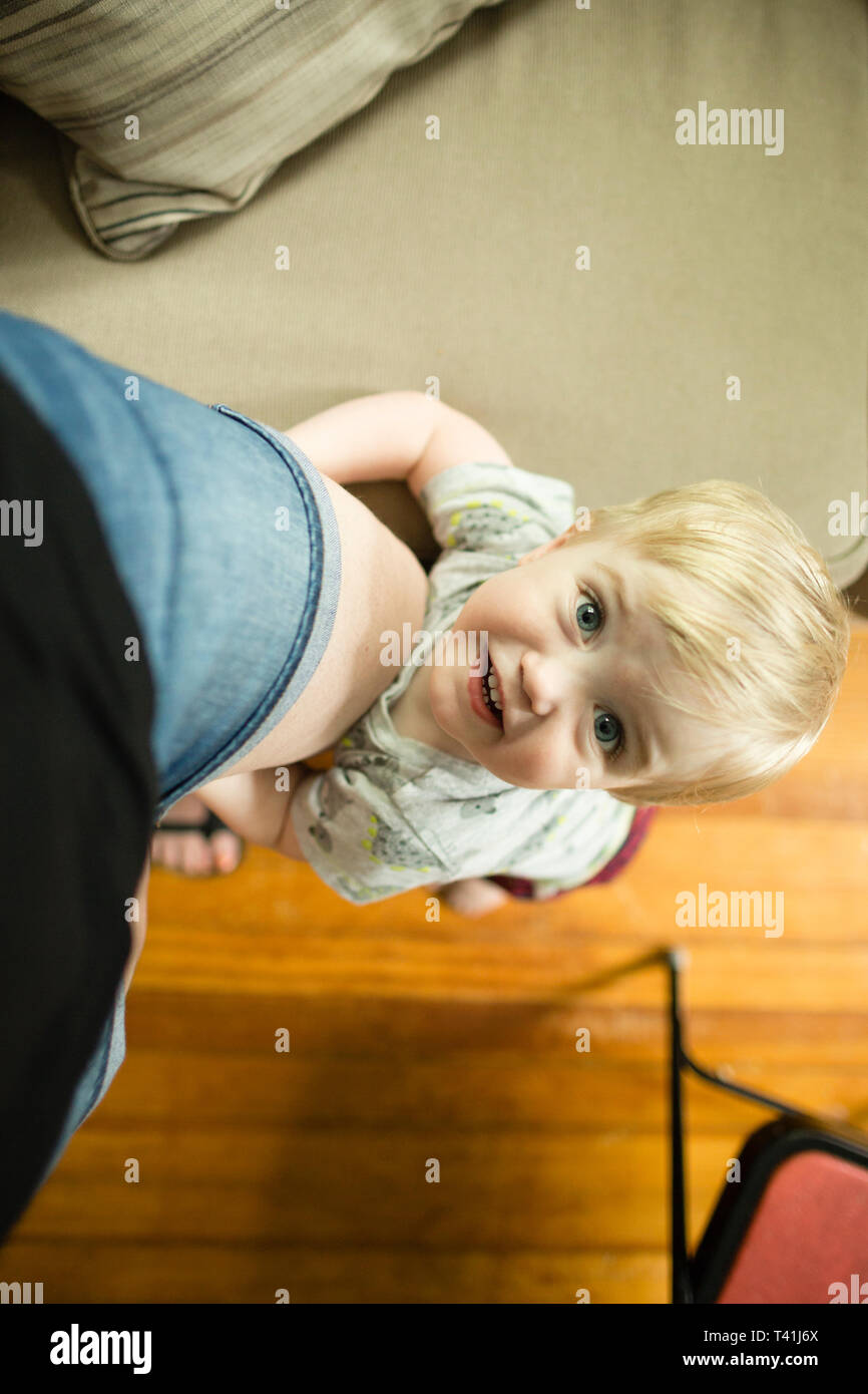 Feliz niño rubio muchacho sostiene en la pierna mientras la madre mirando a la cámara Foto de stock