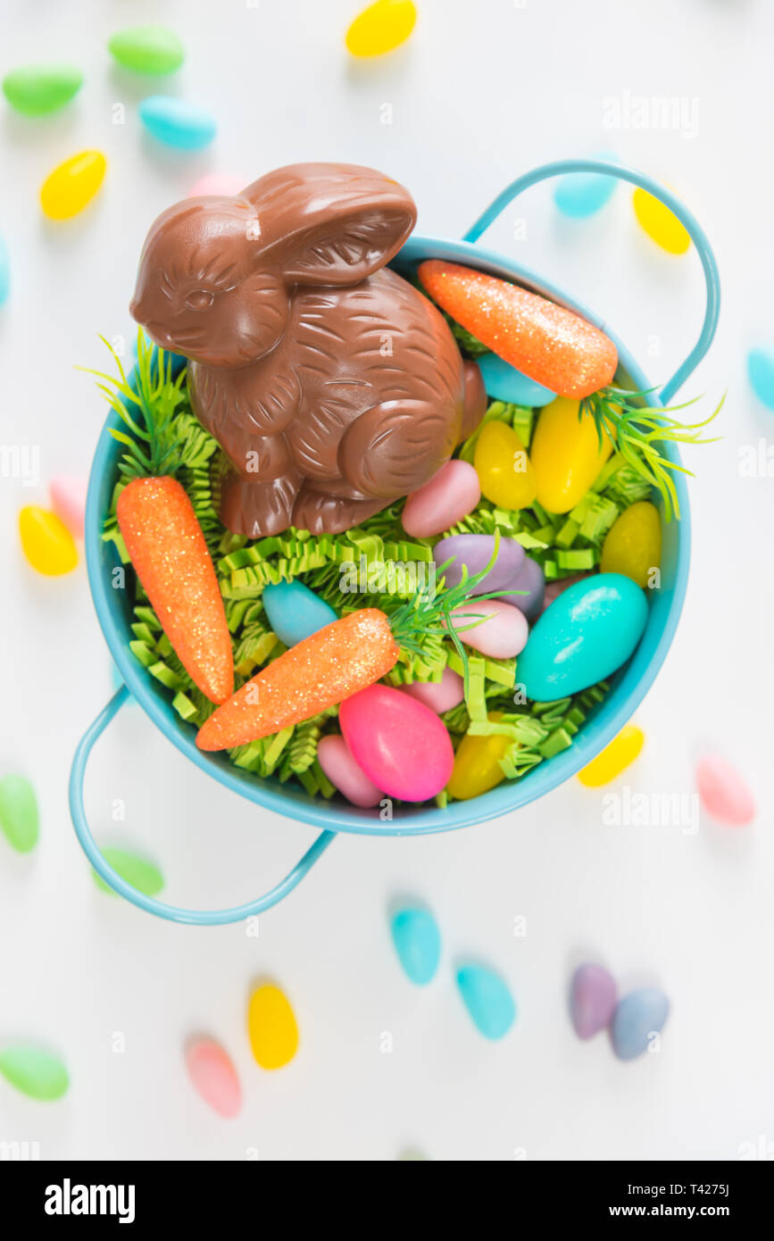 Canasta con conejo de chocolate, dulces, huevos, y mini zanahorias sobre fondo blanco con caramelos Foto de stock