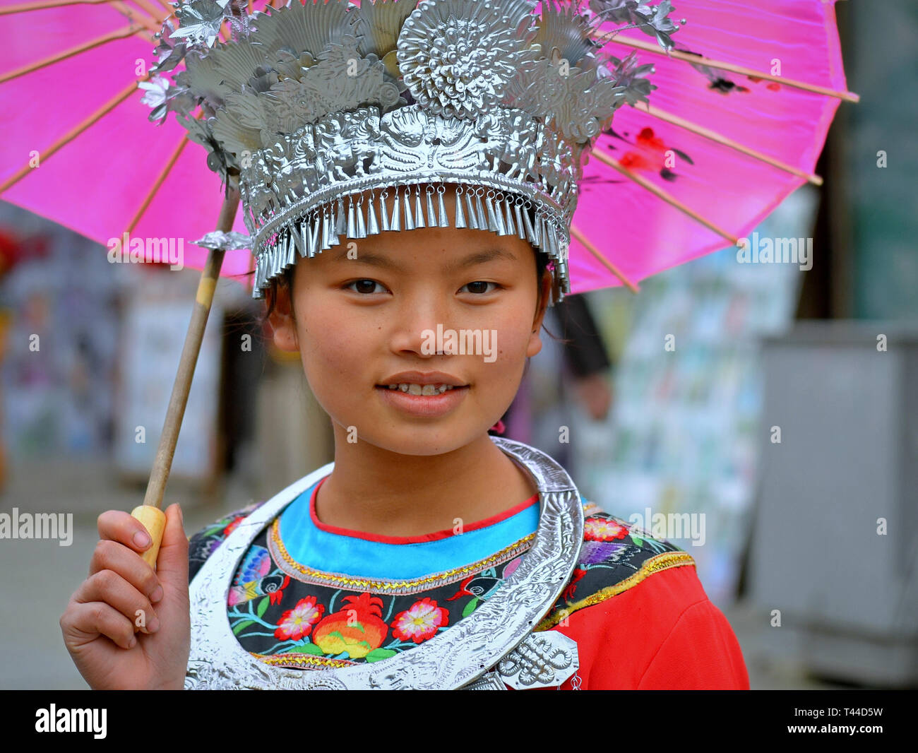 Pre-adolescentes chinos bonita chica con una sombrilla de papel rosa lleva  un tocado Miao tradicional con accesorios de plata y sonrisas para la  cámara Fotografía de stock - Alamy