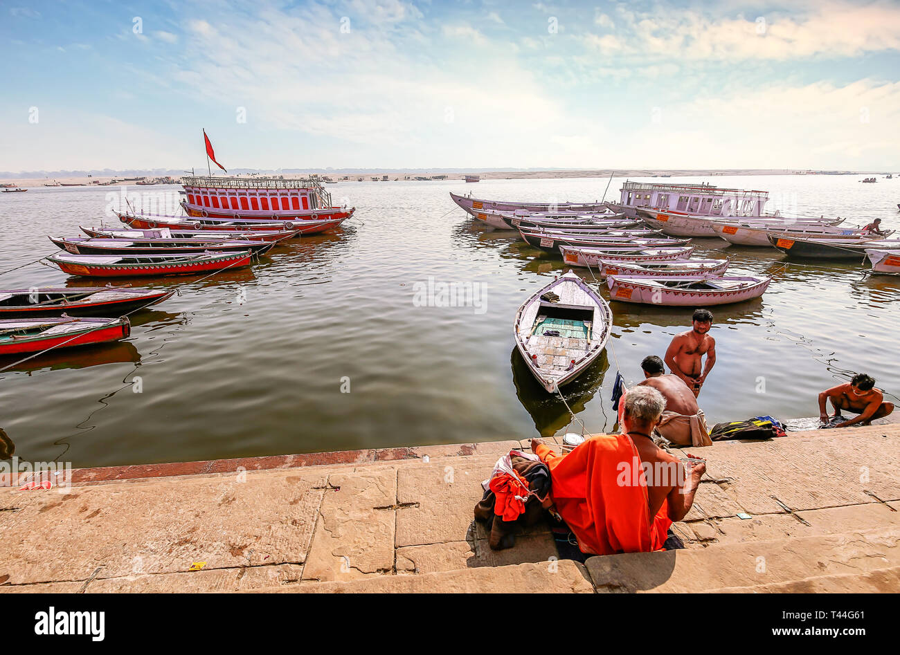 Banco Río Ganges Varanasi con vista de barcos de madera y sadhu baba sentados en la escalera. Foto de stock