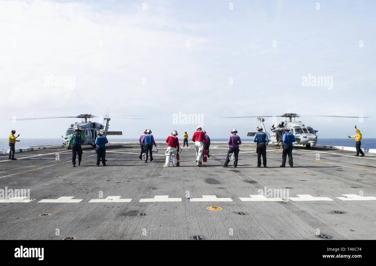 Océano Pacífico (11 de marzo, 2019) - Los marineros asignados al transporte anfibio dock buque USS Green Bay (LPD 20) Preparar al combustible SH-60 Sea Hawk helicópteros asignados a la Isla de los Caballeros de mar escuadrón de helicópteros de combate (HSC) 25 en la cubierta de vuelo durante un ejercicio de entrenamiento con otros buques de guerra de la Marina de los EE.UU. Los buques de guerra de la Marina de EE.UU. entrenan juntos para aumentar la habilidad táctica, la letalidad y la interoperabilidad de las unidades participantes en una época de gran potencia para la competencia. Foto de stock