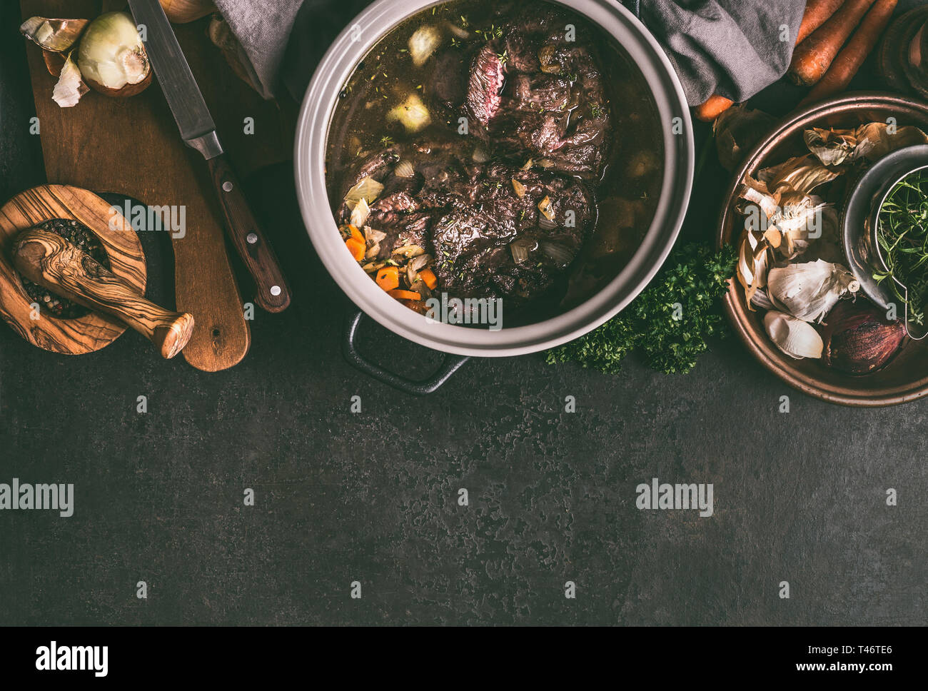 Estofado de Carne de res en la olla cocción en oscuro tabla rústica con  hierbas, especias y utensilios de cocina, vista superior, espacio de copia.  Los platos de carne del país. Cocción