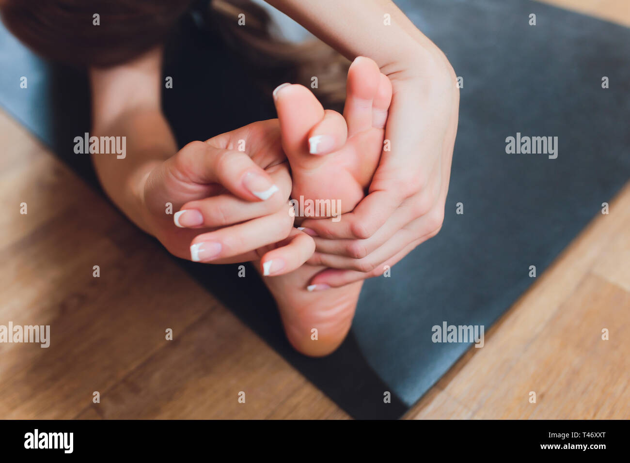 Close-up de una chica haciendo un asana doblarse hacia adelante con sus manos hacia sus piernas. Sentado en el suelo sobre una estera del yoga rosa. Agarre en pagan. Marma Foto de stock