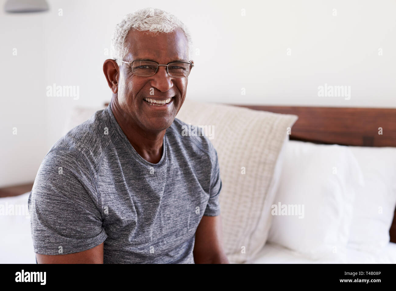 Retrato de Senior sonriente hombre sentado en el lado de la cama, en su casa mirando positivo Foto de stock