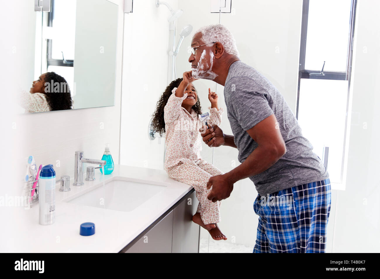 Abuelo vistiendo Pijama en el baño, mientras que la nieta de afeitado relojes Foto de stock