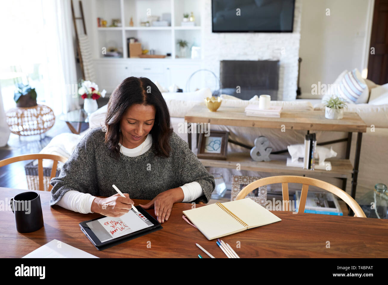 Vista elevada de mediana edad de raza mixta mujer sentada en una mesa en su comedor con un lápiz de tablet pc, vista elevada, centrarse en primer plano Foto de stock