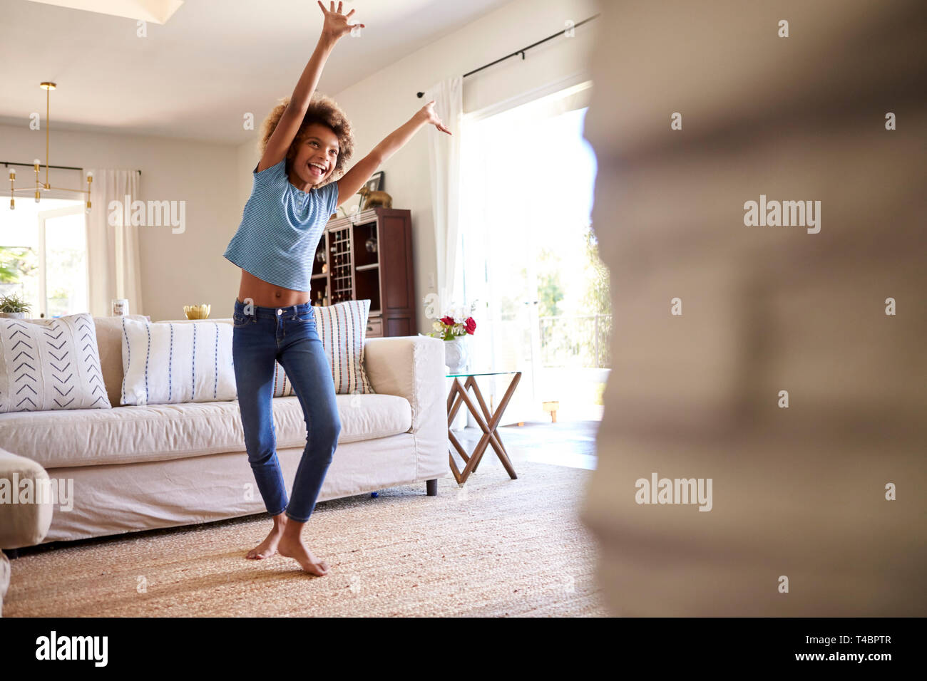 Pre-teen chica bailando y cantando junto a la música en la TV en el salón de su casa, tres cuartos de longitud Foto de stock