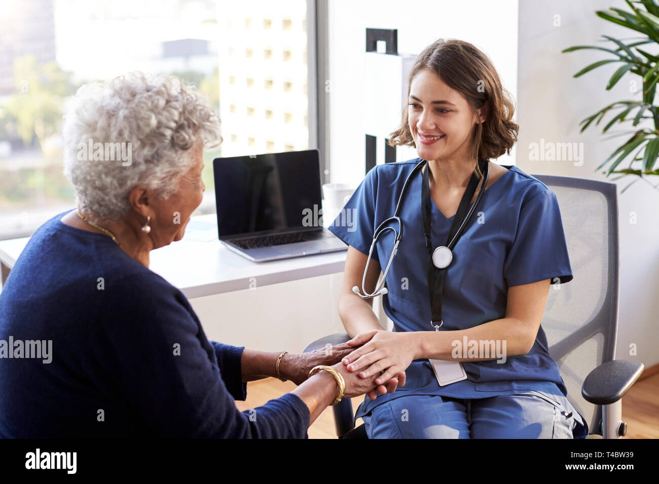 Enfermera vistiendo Scrubs en Office tranquilizador paciente femenino Senior y sosteniendo sus manos Foto de stock