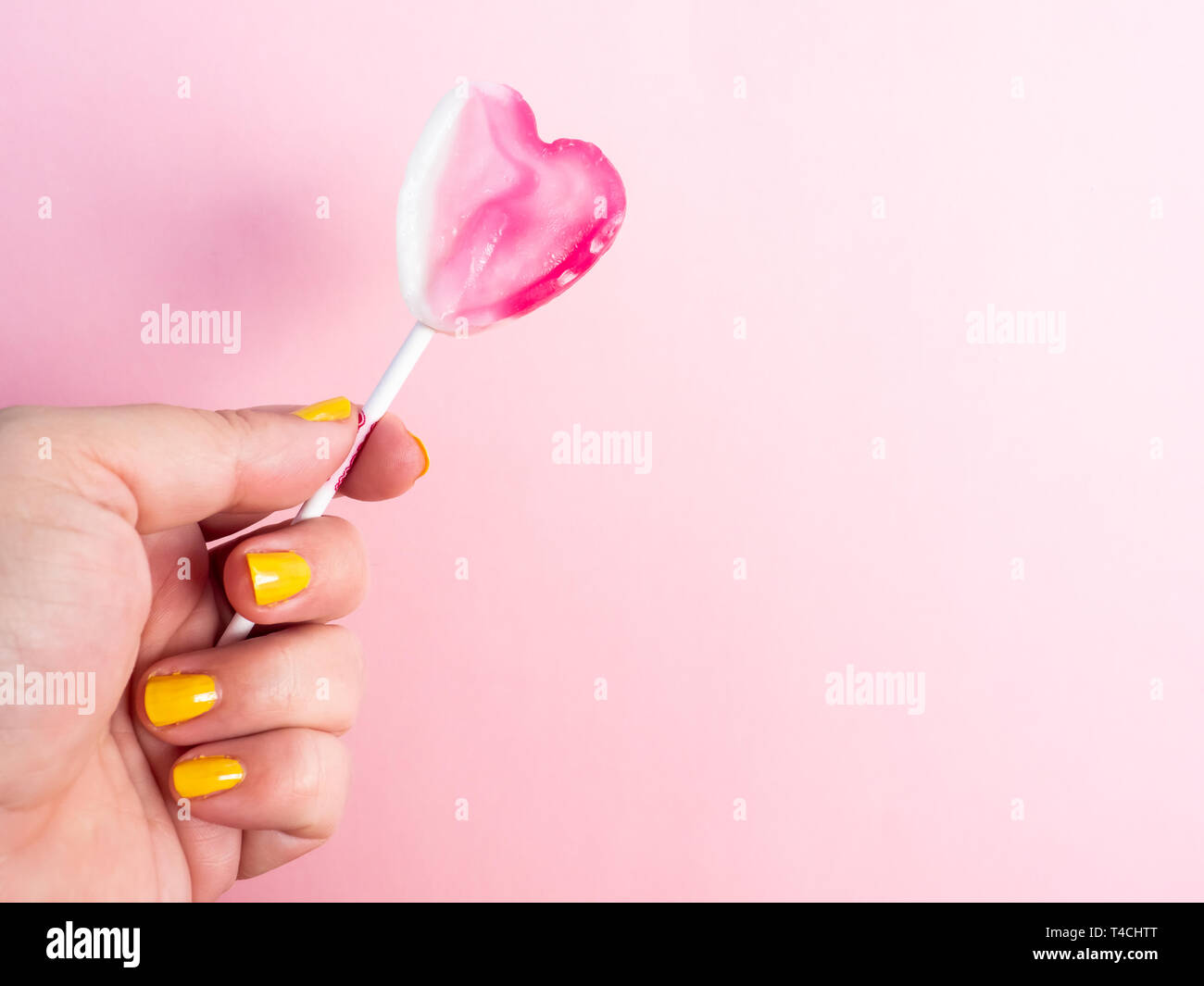 Una mujer con las uñas pintadas en amarillo con un lollipop en su mano y  fondo de color rosa pastel Fotografía de stock - Alamy