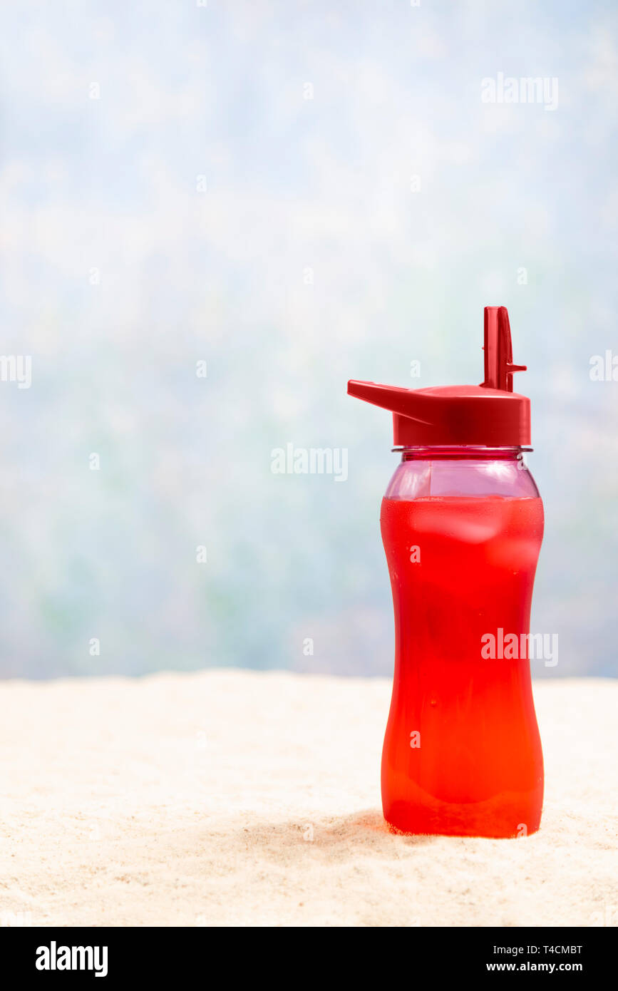 Playa de arena vertical con fondo rojo de bebidas y de poca profundidad de campo. La bebida es de color rojo en la esquina inferior derecha. Copie el espacio. Foto de stock