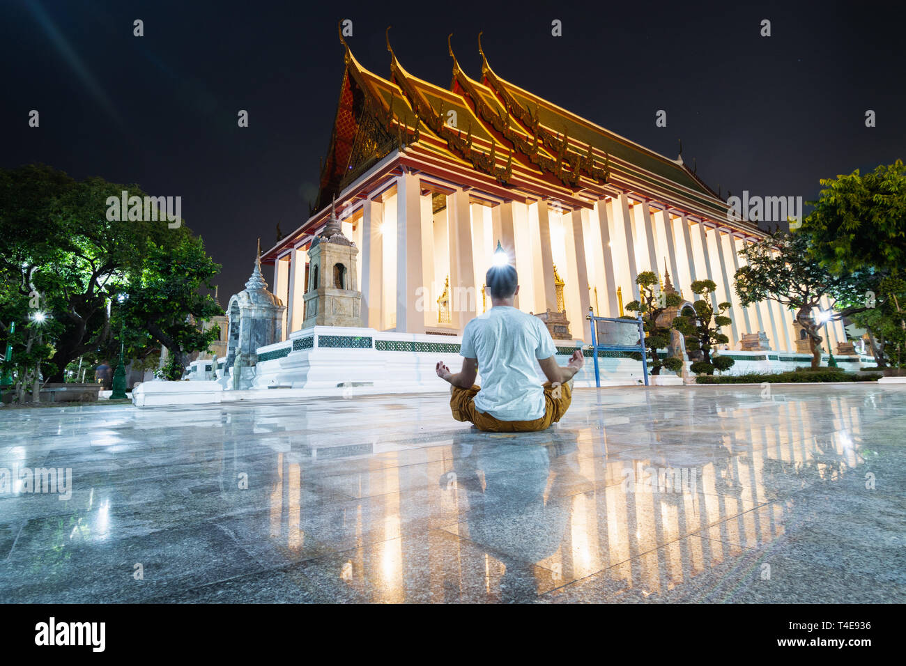 Hombre meditando en lotus plantean en Wat Suthat Thepwararam durante la noche, la reflexión en el suelo baldosas de mármol. Foto de stock