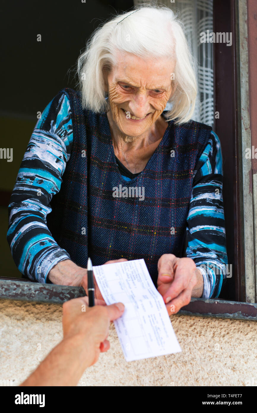 La mujer que recibe cheque de jubilación superiores sobre la ventana en casa Foto de stock