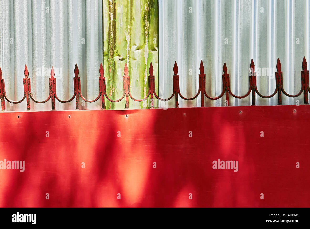 Detalle del diseño de una puerta de metal rojo con flechas soldado adjunta al borde superior, fotografiado contra una pared de planchas de metal corrugado color plata Foto de stock