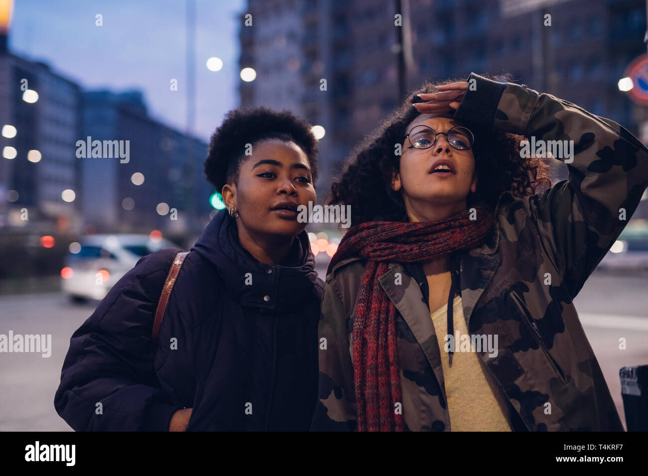 Dos niñas mirando hacia adelante en la ciudad con el cabello rizado y morena - turismo, amistad, expresivo Foto de stock