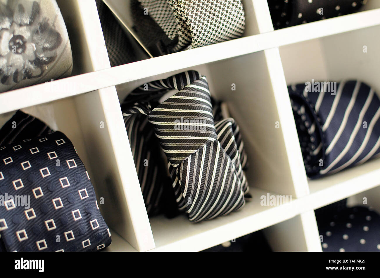 Visualización de corbatas o lazos con patrones clásicos y colores en compartimentos individuales en un gabinete de madera en una tienda de moda para hombres Foto de stock