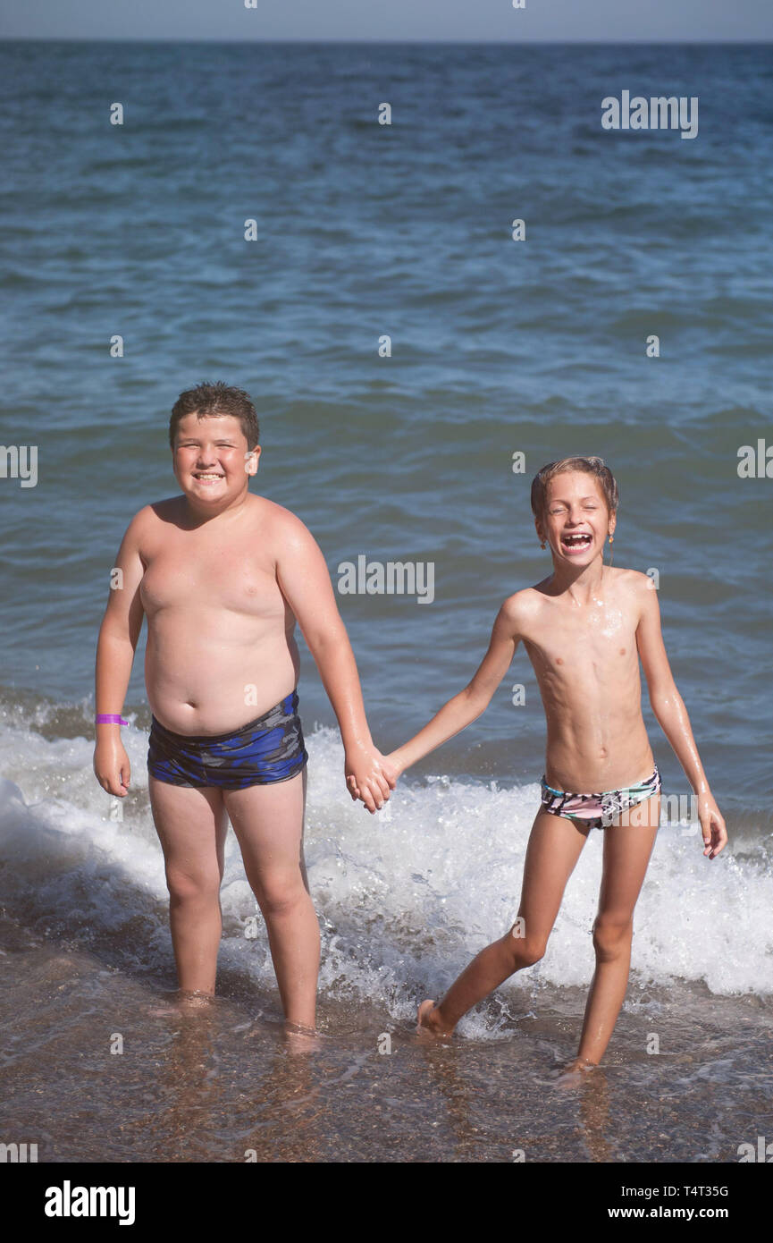 Feliz Fat Boy sonriente sosteniendo la mano de muy delgado riendo niña en la playa durante el verano vacaciones Foto de stock