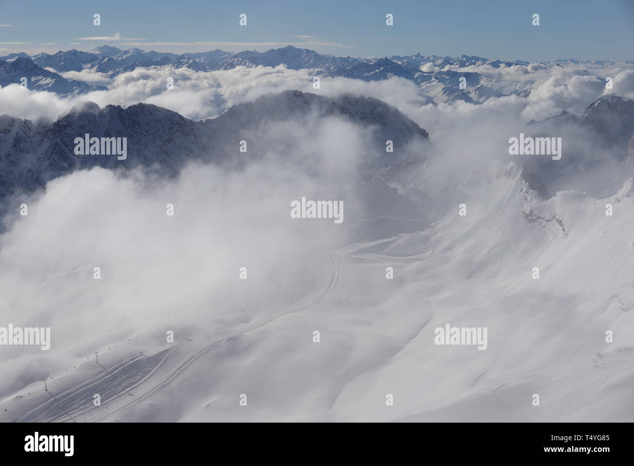 Zugspitze: Blick über einen Gletscher über die Alpen. In den Tälern liegen dichte Wolken. Auf dem Gletscher wabert Nebel. Man erkennt einen Lift und S Foto de stock