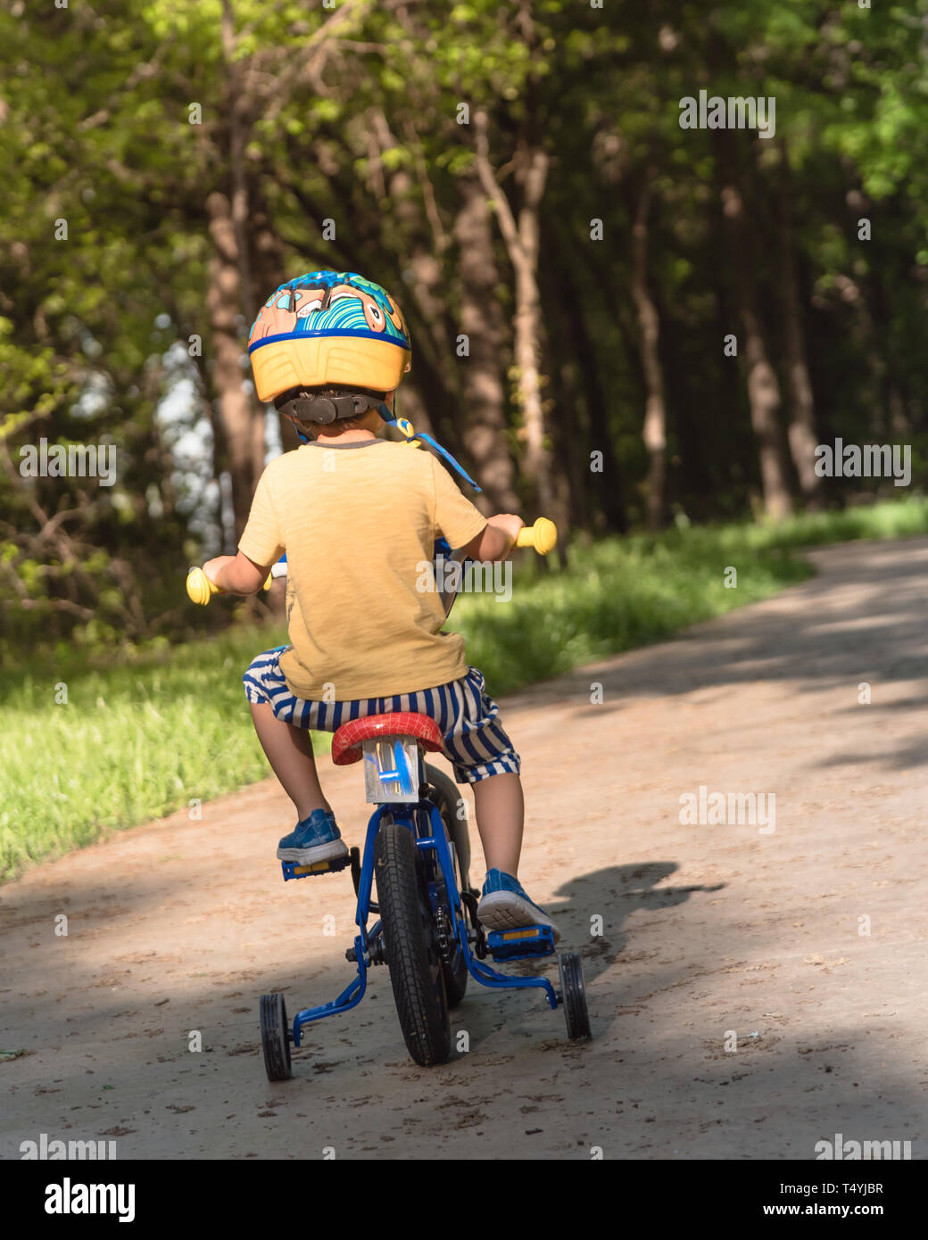 Vista trasera del niño asiático boy triciclo de equitación el parque cerca de Dallas, Texas, EE.UU. Niño Bicicleta con Casco, corto y zapatillas deporte en park conc Fotografía