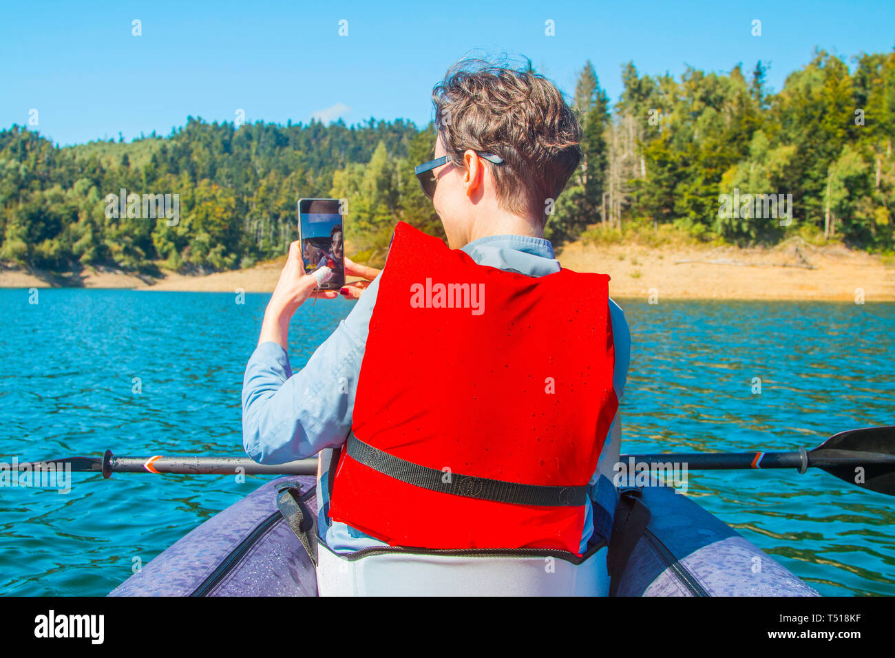 Selfie en el lago. Mujer joven tomando autorretrato con smart phone en kayak en el lago Lokvarsko en Gorski Kotar, Croacia. La mujer disfruta de aventuras Foto de stock