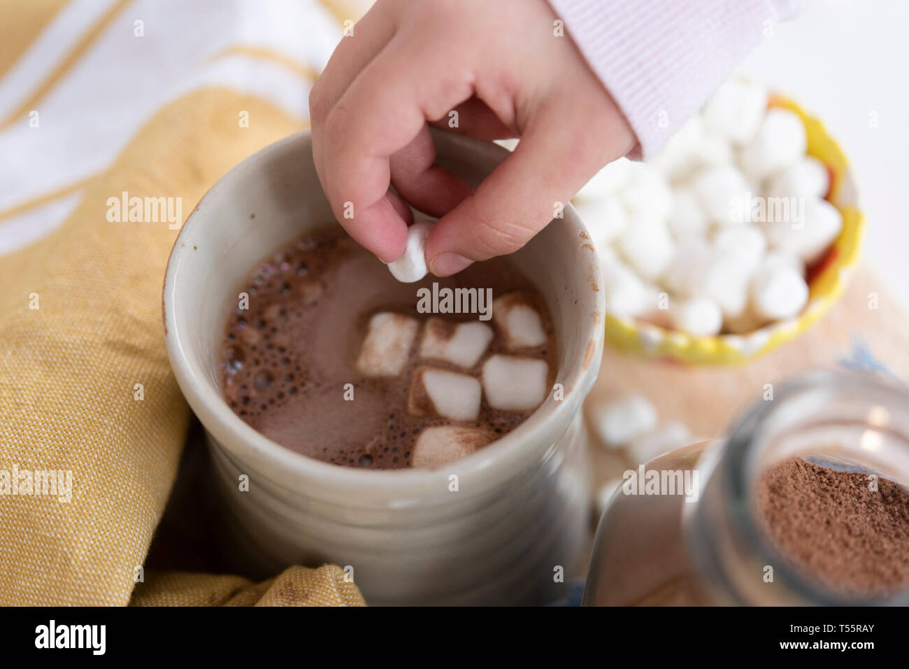 Chica colocando la mano malvaviscos en chocolate caliente Foto de stock