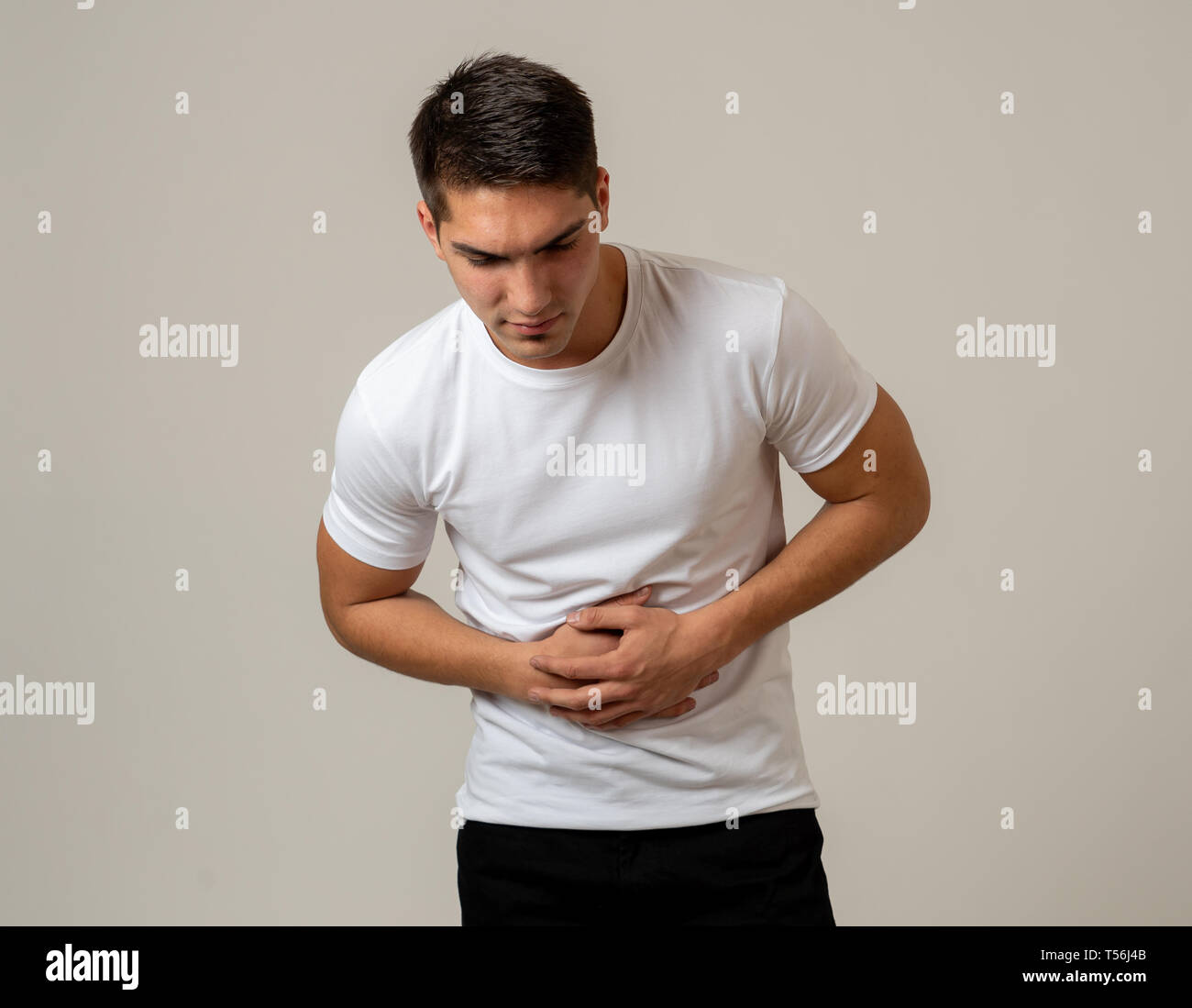 Fitness muscular joven hombre sujetando su estómago sufriendo fuertes dolores abdominales. Aislado sobre fondo neutro. En dolor de estómago, problemas digestivos y Foto de stock