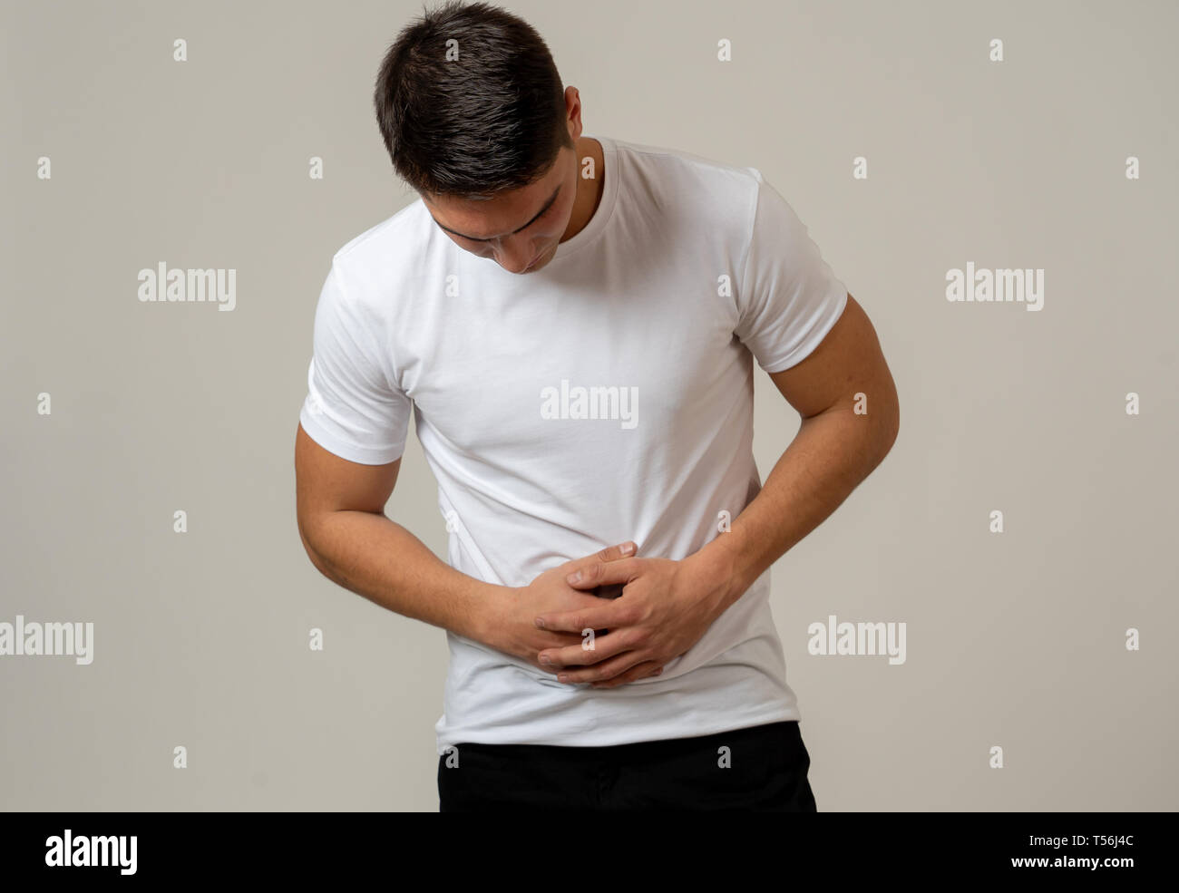 Fitness muscular joven hombre sujetando su estómago sufriendo fuertes dolores abdominales. Aislado sobre fondo neutro. En dolor de estómago, problemas digestivos y Foto de stock