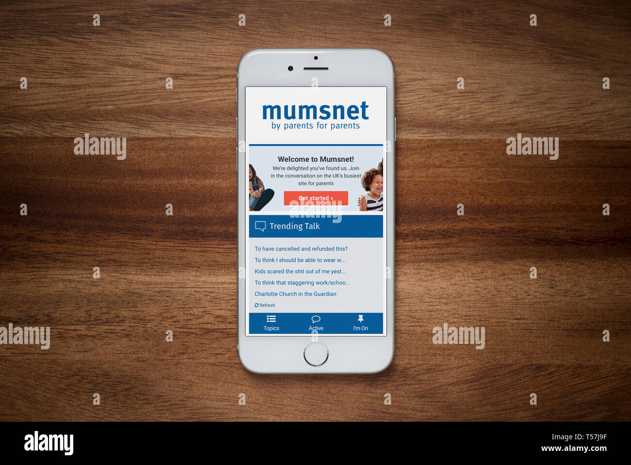 Un iPhone que muestra el sitio web Mumsnet descansa sobre una mesa de madera normal (uso Editorial solamente). Foto de stock