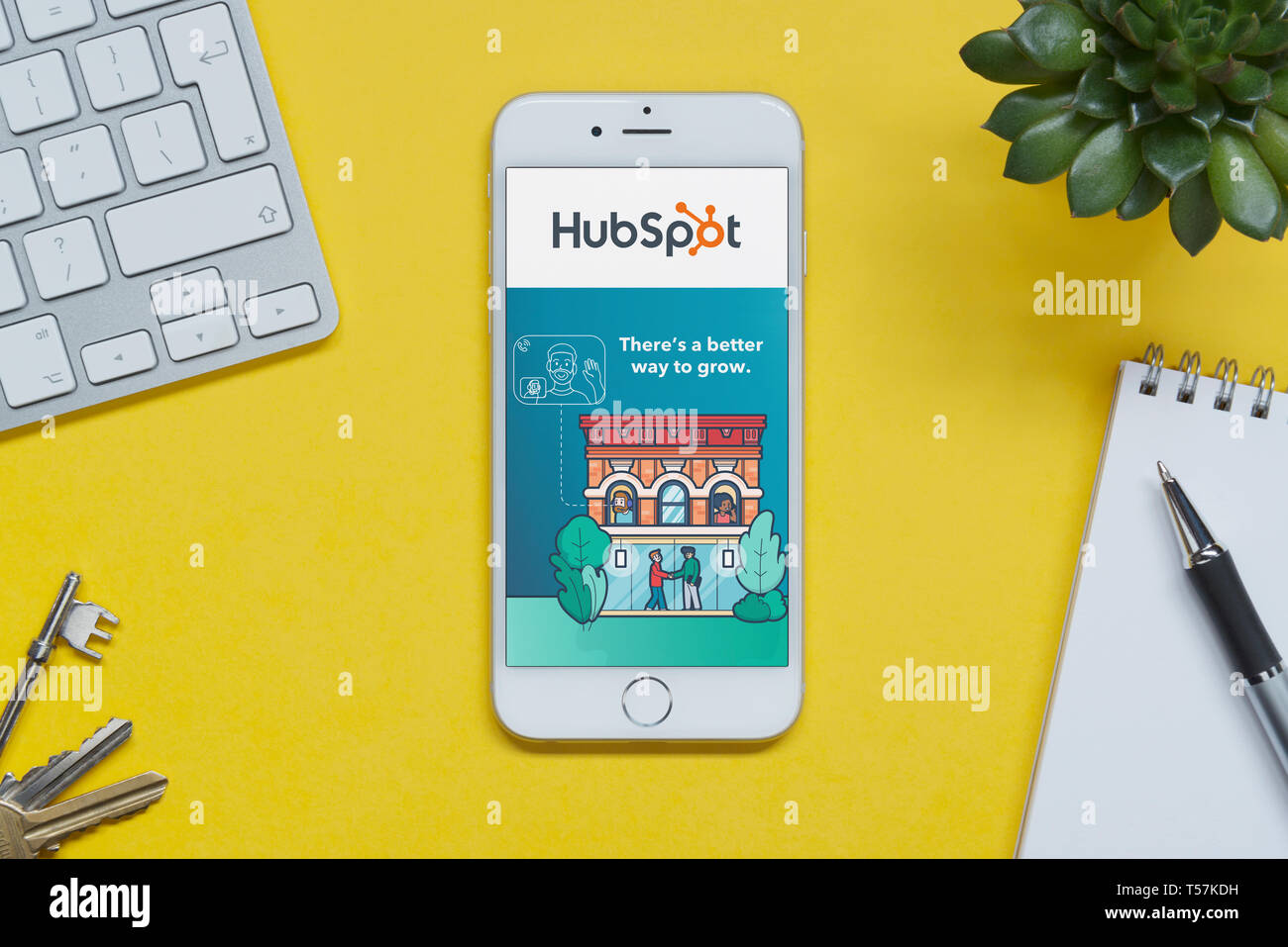 Un iPhone que muestra el sitio web Hubspot descansa sobre un fondo amarillo tabla con un teclado, teclas, bloc de notas y Planta (uso Editorial solamente). Foto de stock