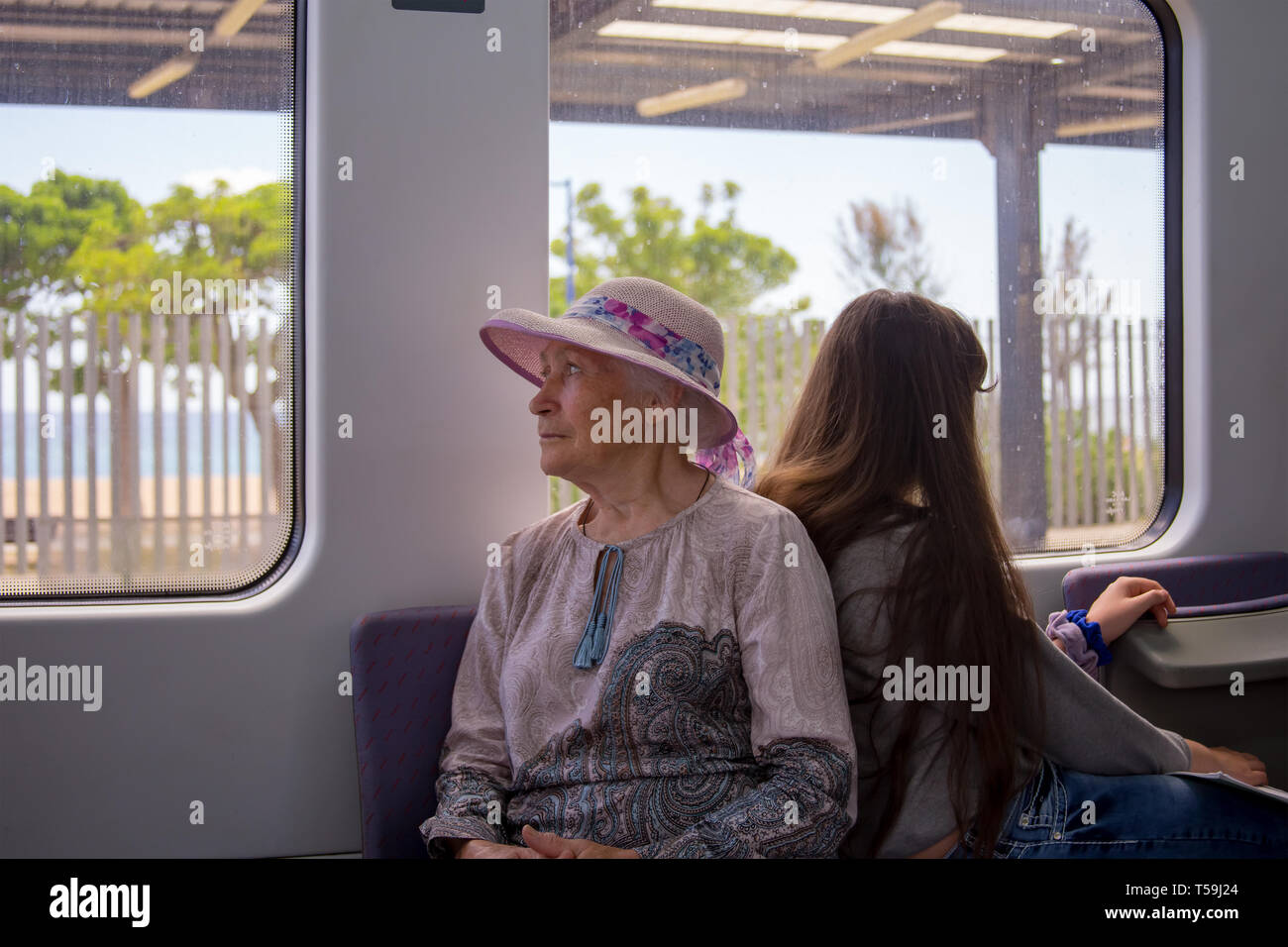 Hermosa abuela de cabellos grises en un sombrero paseos en un tren de cercanías y mira por la ventana. Foto de stock