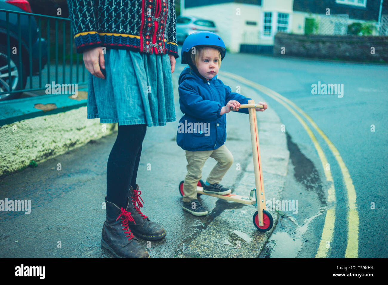 Una Madre Esta De Pie En La Calle Con Su Bebe Que Esta Montando Un Scooter Fotografia De Stock Alamy