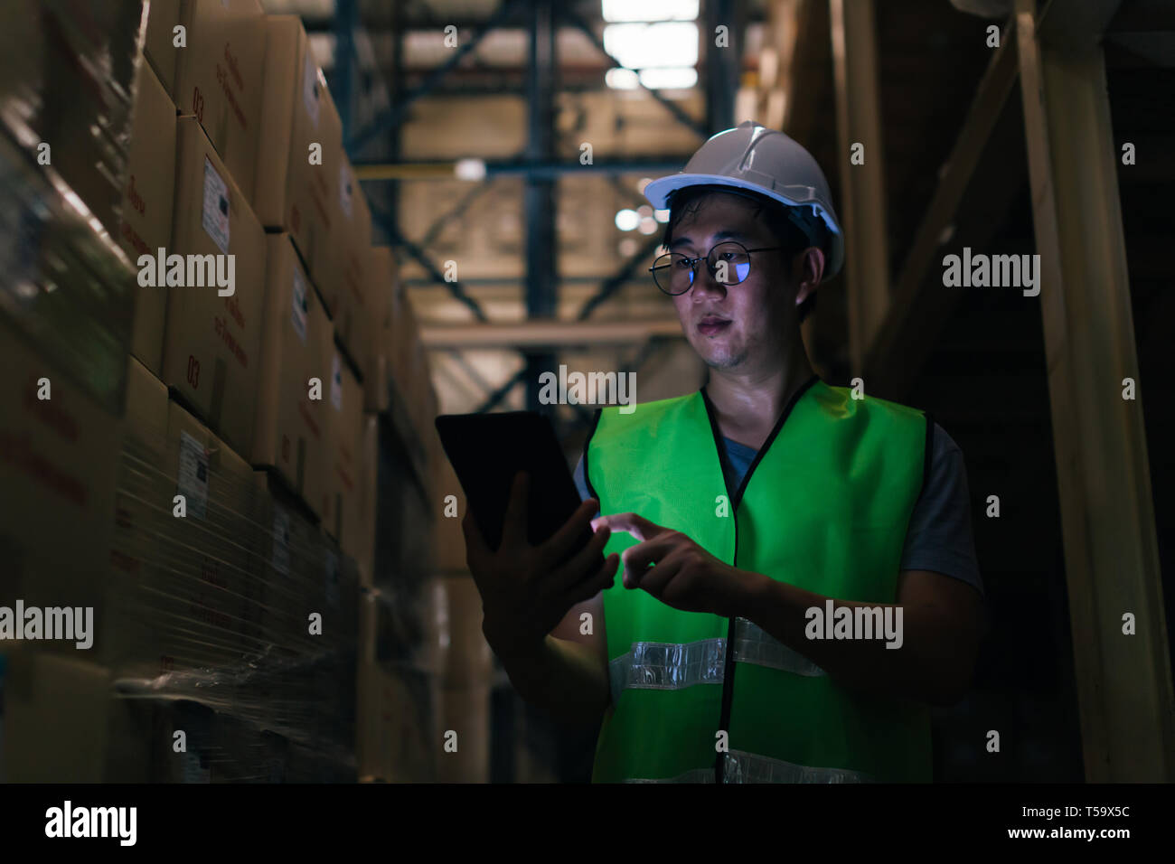 Joven Asiático Masculino trabajador de almacén utilizando una tableta digital dentro del almacén para comprobar el inventario y la gestión de las existencias en la fábrica. Foto de stock