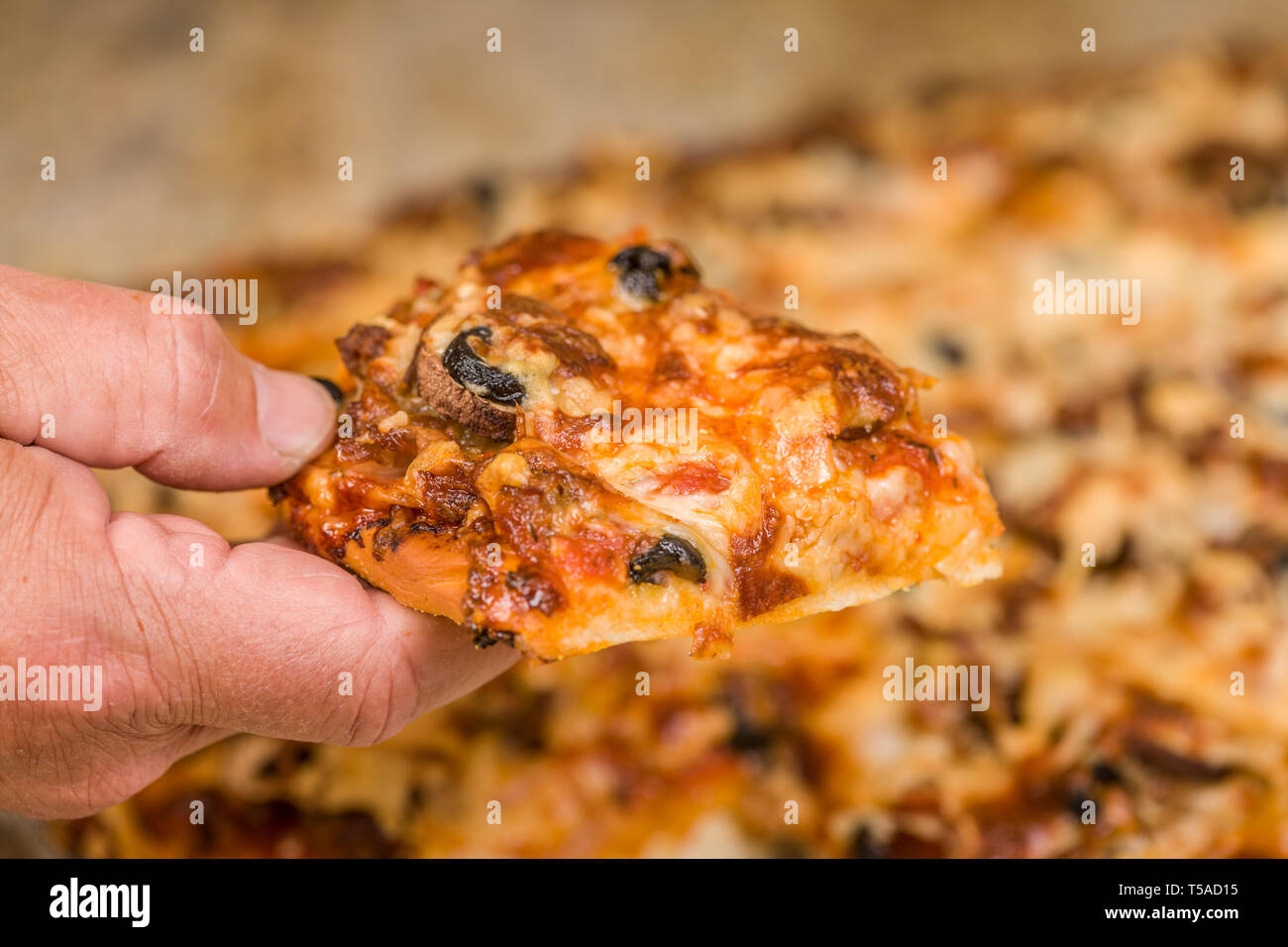 El Hombre recogiendo un trozo de carne y veggie pizza casera con ingredientes de salchichas, salchichones, tocino canadiense, aceitunas negras, champiñones, mozzarella chee Foto de stock