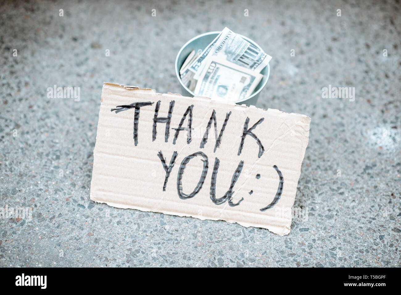 Beggar's cup con dinero y cartón con mensaje de agradecimiento en la calle Foto de stock