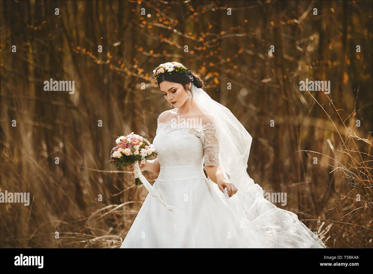 Elegante Y Joven Morenita Mujer Con Maquillaje Y Brillante Con Una Corona De Flores En La Cabeza En Un Elegante Vestido De Novia Con Un Ramo De Flores Al Aire Libre Fotografia