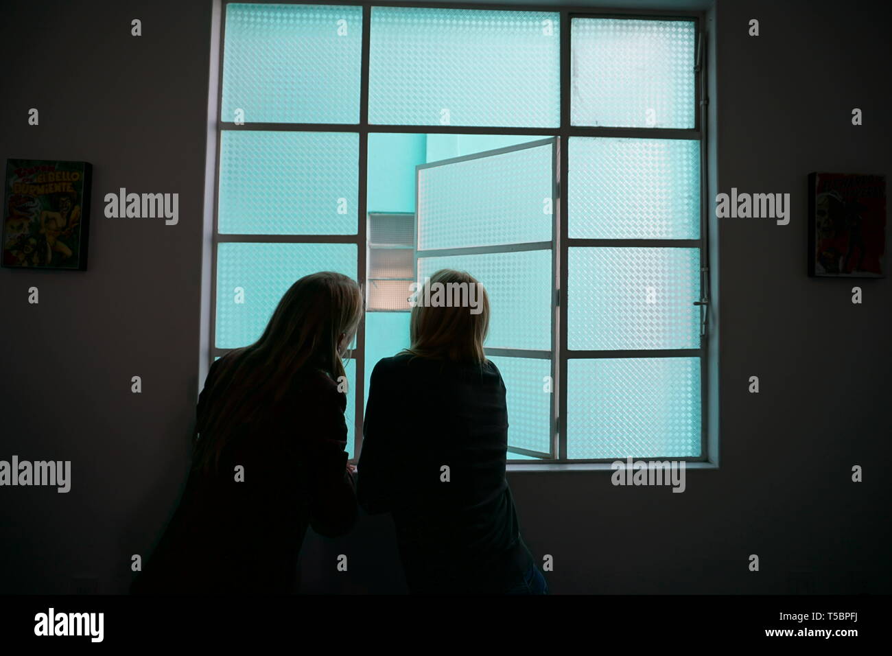 Silueta de la mujer y la niña mirando por la ventana de vidrio esmerilado, ventana de color turquesa. Foto de stock