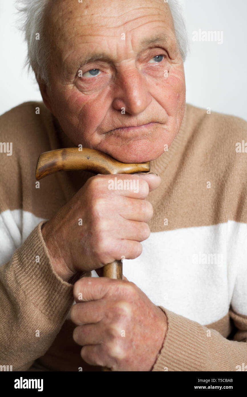 Retrato de un viejo triste hombre que puso su cabeza sobre el mango de un bastón de madera, el concepto de soledad en casa. Foto de stock