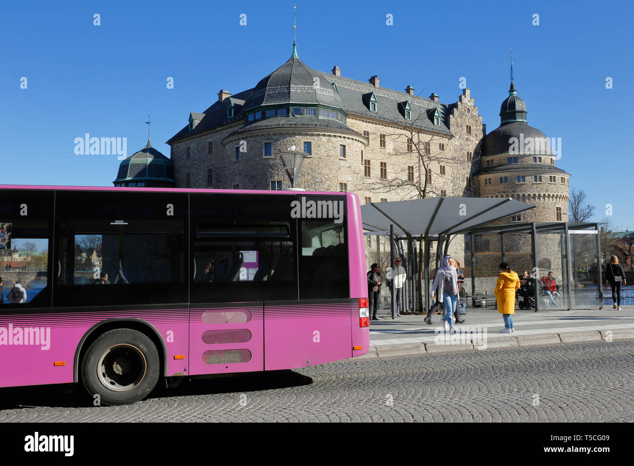 Orebro, Suecia - 17 de abril de 2019: Una violeta ciudad transporte público bus enfrente del castillo de Örebro. Foto de stock