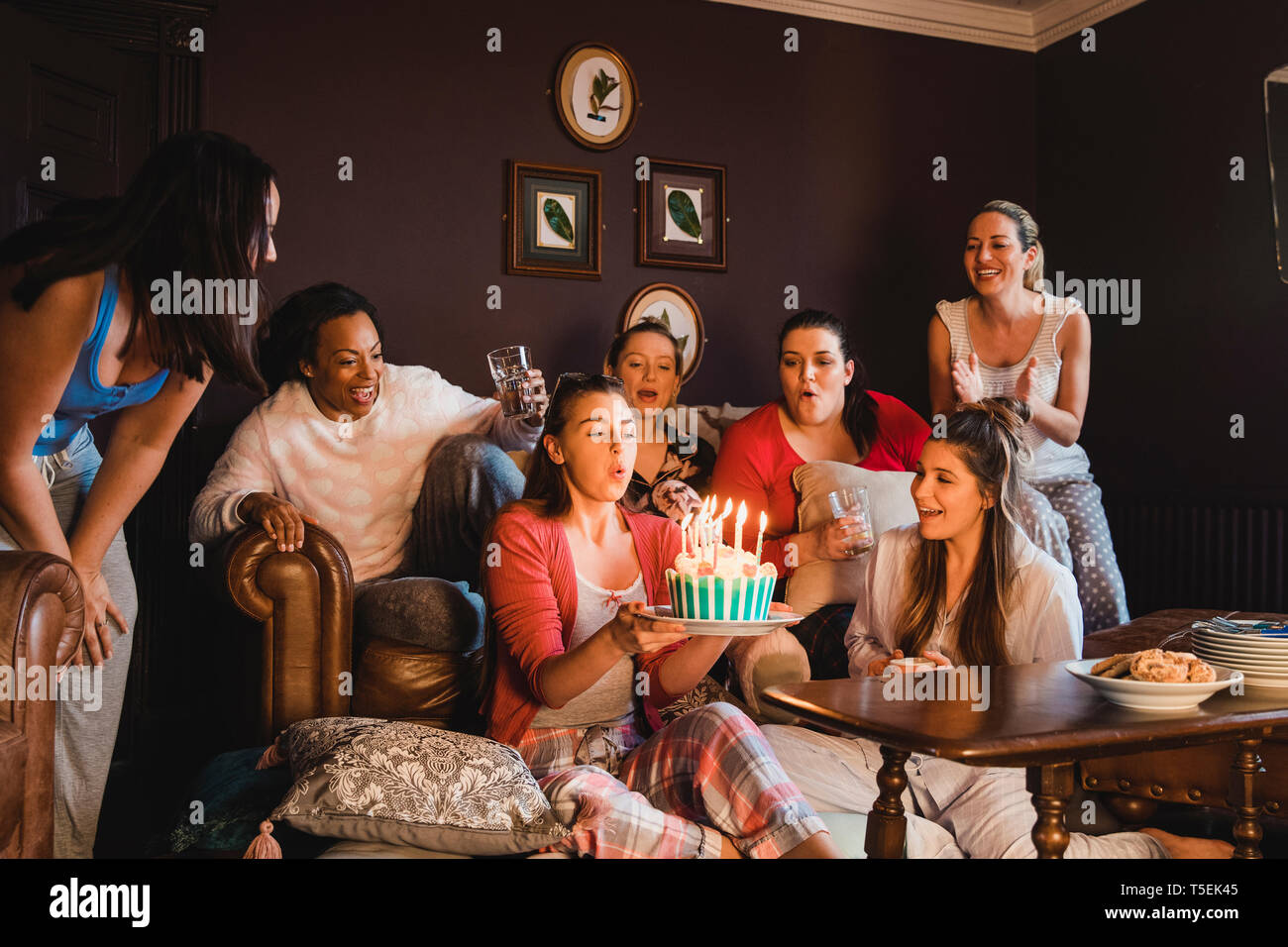 Un pequeño grupo de amigas celebrando un cumpleaños con un pastel de cumpleaños mientras se relaja en casa. Foto de stock